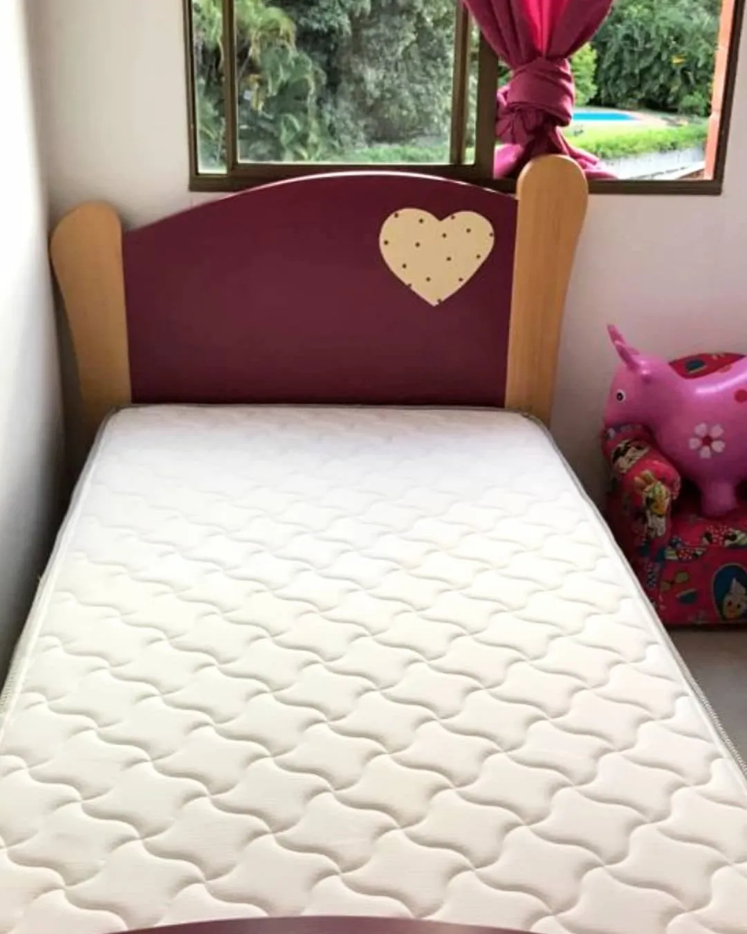 Cama individual con cabecero vinotinto, en un cuarto con vista al jardín